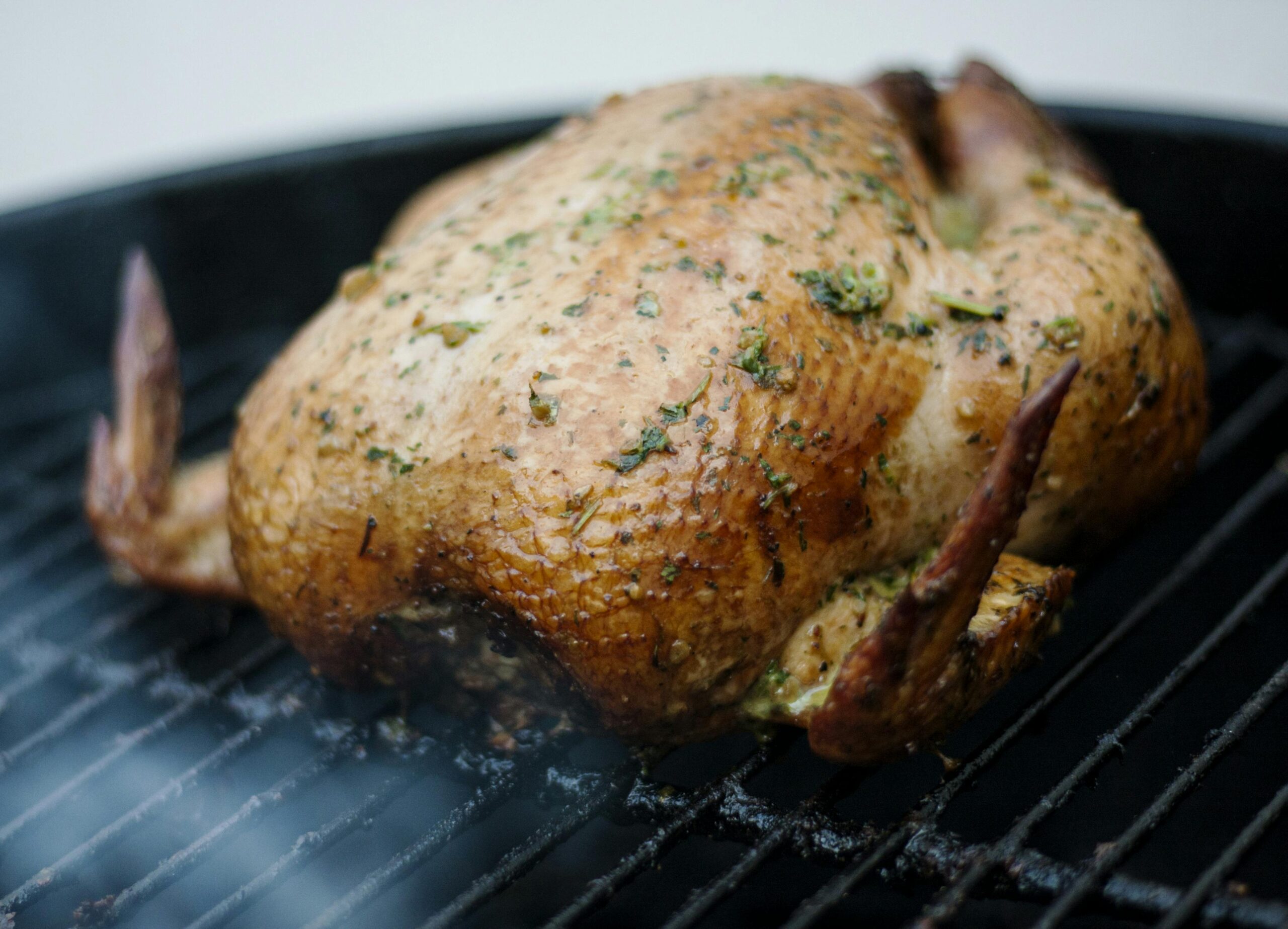 Whole chicken seasoned with herbs, grilled to perfection on a barbecue grill.